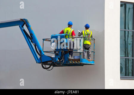 Two plasterers finishing off a wall on a lift platform Stock Photo