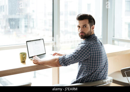 Picture of young handsome man in office coworking while using laptop computer. Looking at camera. Stock Photo