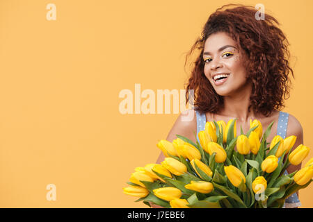 Beauty African woman holding bouquet of flowers and looking at the camera over yellow background Stock Photo