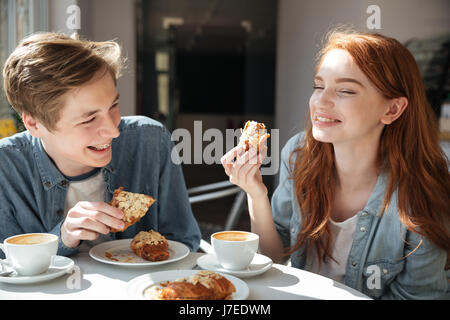 Pretty couple of laughing students eating croissants in cafe Stock Photo