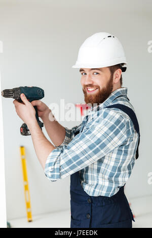 Young bearded man in helmet using drill to make repair isolated Stock Photo