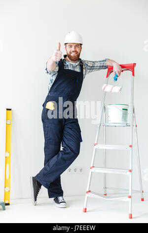 Young man leaning on ladder and showing thumb up while making repair isolated Stock Photo