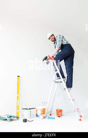 Picture of young smiling man builder standing indoors in new flat and make repair. Looking at camera. Stock Photo