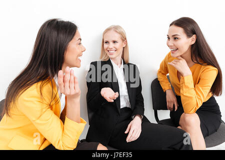 Image of a group of happy colleagues women sitting in office talking with each other. Looking aside. Stock Photo