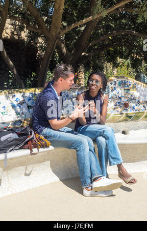 A man and a woman sitting on a mosaic tiled bench on the terrace at Antoni Gaudi's Park Güell, Barcelona, Spain Stock Photo