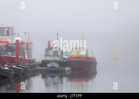 A foggy summers morning on the River Dee with boats fading into the mist whilst moored together in the city of Chester, Cheshire, England, UK Stock Photo