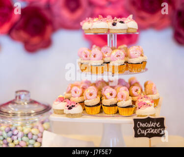 Mini chocolate cupcakes topped with mini pink donuts on a dessert table. They are displayed on a tiered display tray. There is a cute chalkboard sign. Stock Photo
