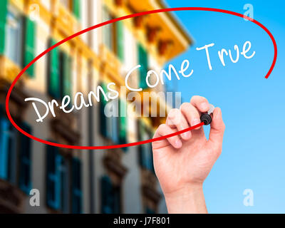 Man Hand writing Dreams Come True with black marker on visual screen. Isolated on city. Business, technology, internet concept. Stock Photo Stock Photo