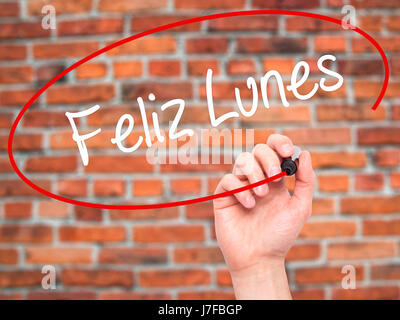 Man Hand writing Feliz Lunes (Happy Monday In Spanish) with black marker on visual screen. Isolated on bricks. Business, technology, internet concept. Stock Photo