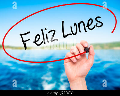 Man Hand writing Feliz Lunes (Happy Monday In Spanish) with black marker on visual screen. Isolated on nature. Business, technology, internet concept. Stock Photo