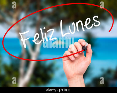 Man Hand writing Feliz Lunes (Happy Monday In Spanish) with black marker on visual screen. Isolated on nature. Business, technology, internet concept. Stock Photo