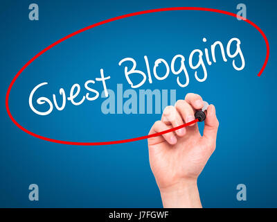 Man Hand writing Guest Blogging  with black marker on visual screen. Isolated on blue. Business, technology, internet concept. Stock Photo Stock Photo