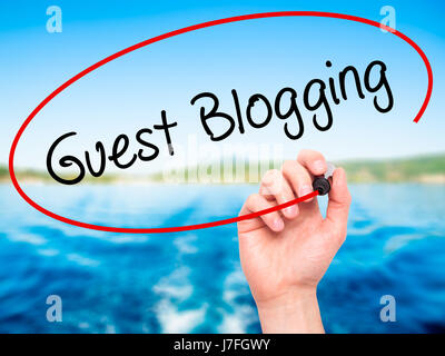 Man Hand writing Guest Blogging  with black marker on visual screen. Isolated on nature. Business, technology, internet concept. Stock Photo Stock Photo