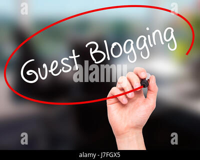 Man Hand writing Guest Blogging  with black marker on visual screen. Isolated on office. Business, technology, internet concept. Stock Photo Stock Photo
