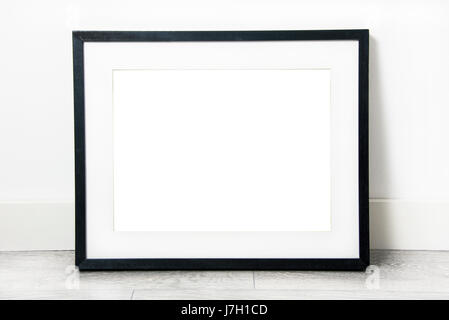Black rectangular frame with mat, blank inside, leaning against wall on grey oak flooring Stock Photo