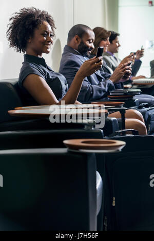 African American woman or businesswoman using cell phone in busy airport with other people in background Stock Photo