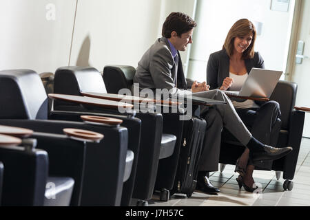 Man and woman, businessman and businesswoman sitting in chairs using laptop in business meeting at airport Stock Photo