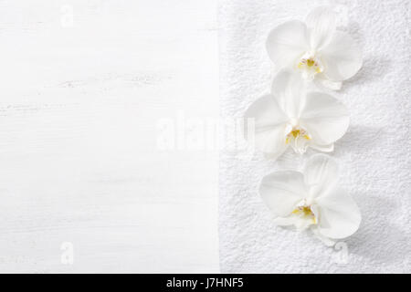 Three orchids and white terry towel  lying on shabby wooden board.  Viewed from above. Spa concept. Stock Photo