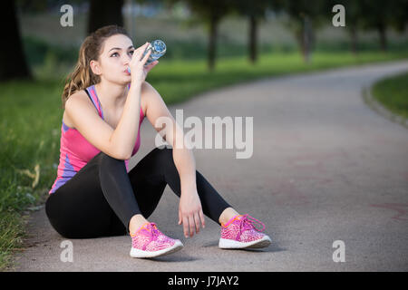 Thirsty woman drinking water to recuperate after jogging Stock Photo