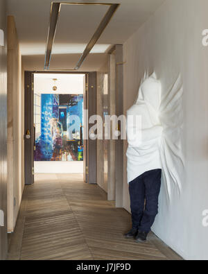 Shrouded figure sculpted from powdered glass by Daniel Arsham in hallway with painting by Oliver Masmonteil Stock Photo