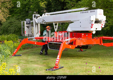 Self propelled cherry picker with extendable legs and caterpillar tracks being used to cut branches from trees Stock Photo