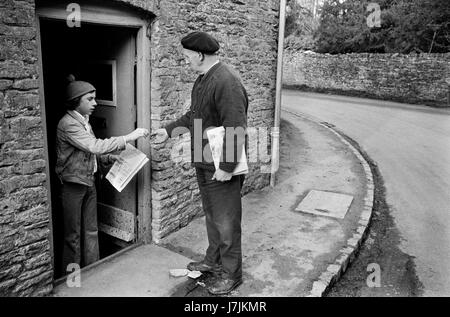 Senior man delivering newspapers in the village Sunday morning delivery. 1970s Britain UK. Village life, keeping busy and fit. The Cotswolds. Lower and Upper Slaughter are twin villages on the River Eye and are know as The Slaughters.  1975 HOMER SYKES Stock Photo