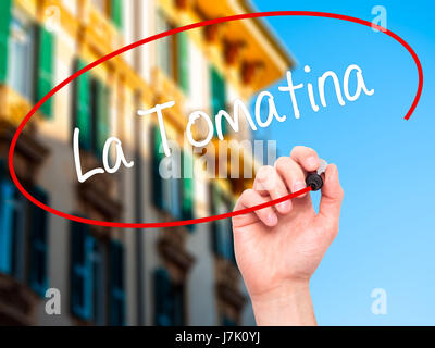 Man Hand writing La Tomatina with black marker on visual screen. Isolated on city. Business, technology, internet concept. Stock Photo