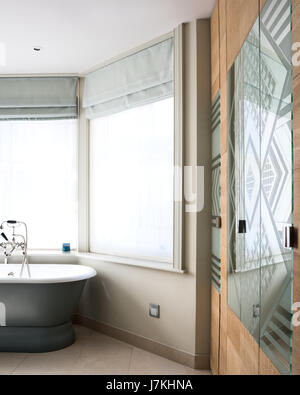 Patterned mirror glass in bathroom with free standing bath and inbuilt cupboards Stock Photo