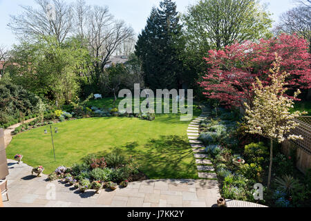 Suburban garden with paved walkway, lawn and assorted planting schemes. Stock Photo