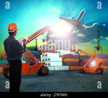 working man in logistic business working in container shipping yard with dusky sky and jet plane cargo flying above use for land to air transport and  Stock Photo
