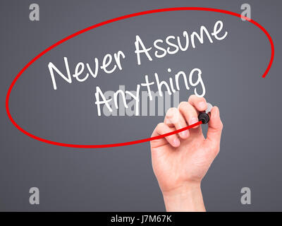 Man Hand writing Never Assume Anything with black marker on visual screen. Isolated on grey. Business, technology, internet concept. Stock Photo Stock Photo
