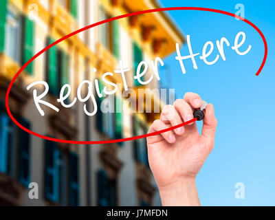 Man Hand writing Register Here with black marker on visual screen. Isolated on city. Business, technology, internet concept. Stock Photo Stock Photo