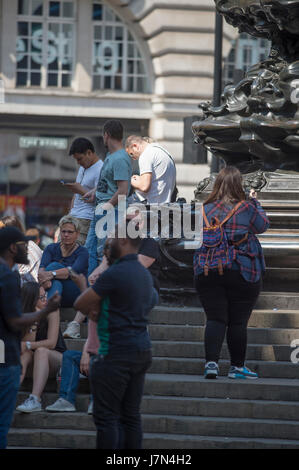 London, UK. 25th May 2017. Commuters and tourists enjoy hot sunshine and high temperatures this morning. Tourists in cool shade at Eros in Piccadilly Circus. Credit: Malcolm Park editorial/Alamy Live News. Stock Photo