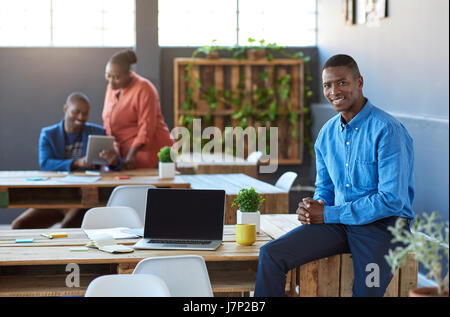 African businessman sitting on his desk with colleagues in background Stock Photo