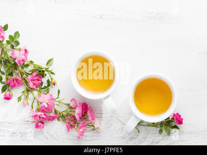 Two cups  of tea and branch of small pink roses on rustic table. Stock Photo