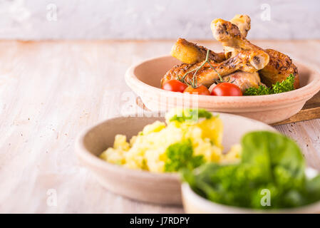 Horizontal photo with three bowls. First contains baked chicken legs with crunchy skin, parsley and tomatoes. Second meshed herb potatoes and one with Stock Photo