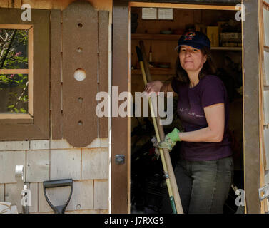 Woman holding garden tools in doorway of garden shed Stock Photo