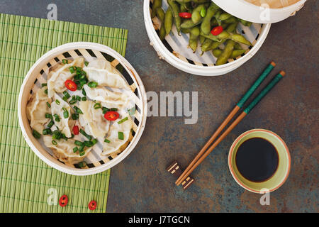 Streamed Gyoza (Jiaozi) and Edamame beans served warm with salt in bamboo steamer. Top view, blank space Stock Photo