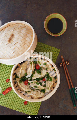 Gyoza potstickers or dumplings in bamboo steamer with sliced spring onion and ponzu dipping sauce. Top view, blank space Stock Photo