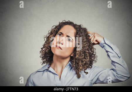 Closeup portrait young woman scratching head, thinking daydreaming about something wondering looking up isolated on grey wall background. Human facial Stock Photo