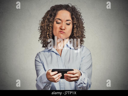 Portrait young angry woman unhappy, annoyed by something, someone on her cell phone while texting, receiving bad sms text message isolated grey wall b Stock Photo