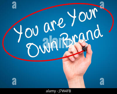 Man Hand writing You are Your Own Brand with black marker on visual screen. Isolated on blue. Business, technology, internet concept. Stock Image Stock Photo