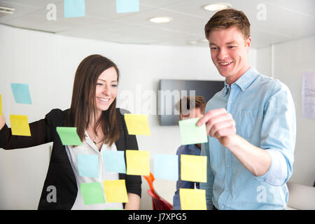 Executives Discussing Over Notes Stuck On Glass In Office Stock Photo