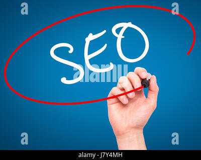 Man Hand writing SEO with marker on transparent wipe board. Isolated on blue. Business, internet, technology concept. Stock Photo Stock Photo