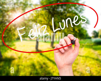 Man Hand writing Feliz Lunes (Happy Monday In Spanish) with black marker on visual screen. Isolated on nature. Business, technology, internet concept. Stock Photo