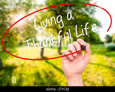 Man Hand writing Living a Thankful Life with black marker on visual screen. Isolated on nature. Business, technology, internet concept. Stock Photo