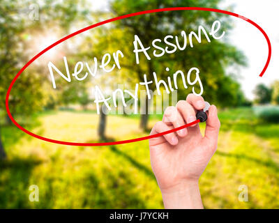 Man Hand writing Never Assume Anything with black marker on visual screen. Isolated on nature. Business, technology, internet concept. Stock Photo Stock Photo