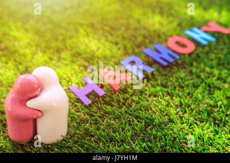 White and pink ceramic doll on green grass with wood text 'HARMONY' word. Use for harmony day concept Stock Photo
