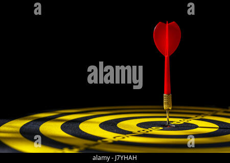 Close up red dart arrow in the center of dartboard. Isolated on black background Stock Photo