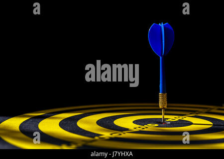 Close up blue dart arrow in the center of dartboard. Isolated on black background Stock Photo